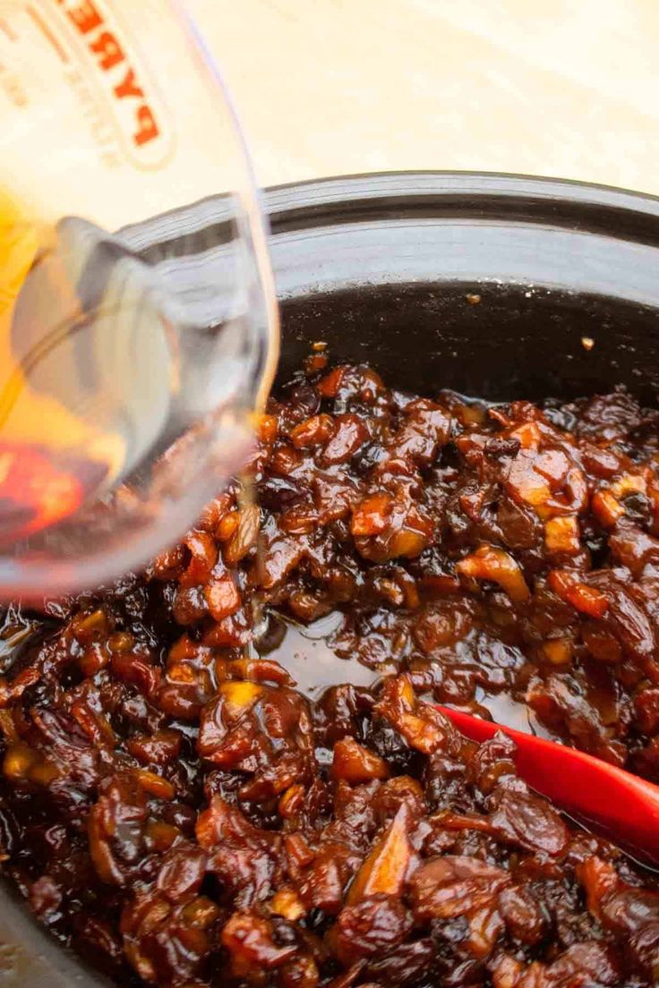 someone pouring wine into a pot filled with food