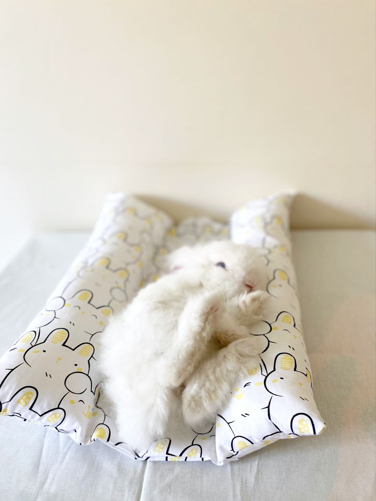 a white stuffed animal laying on top of a bed next to a pillow covered in yellow and white sheets