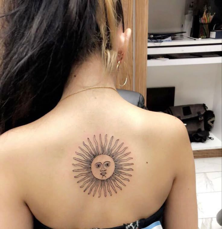 a woman with a sun and moon tattoo on her upper back shoulder, looking at the camera