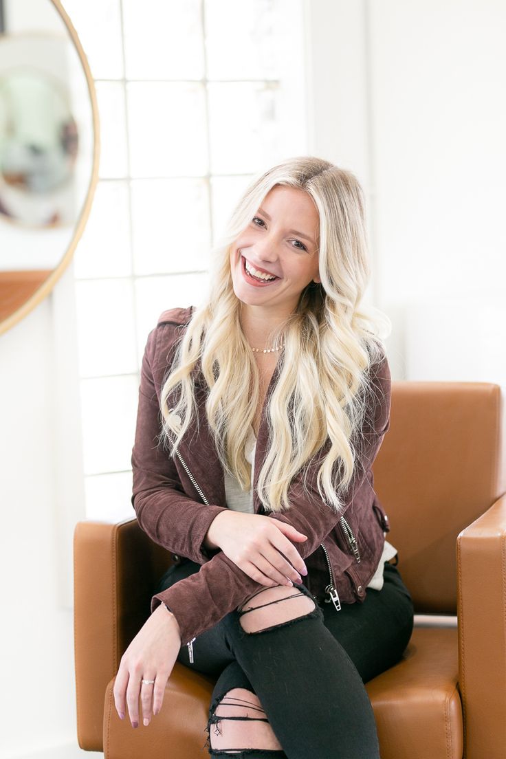 a woman sitting on top of a brown chair in front of a mirror and smiling