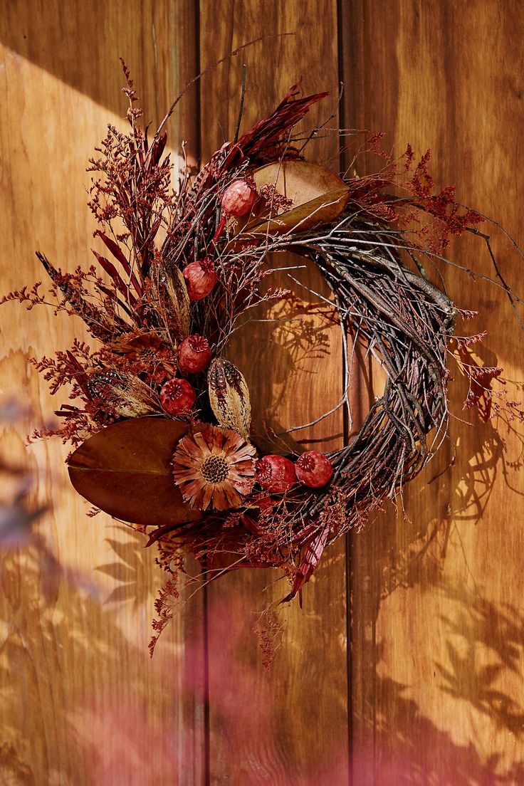 a wreath with dried flowers and leaves hanging on a wooden door frame, in front of a wood paneled wall