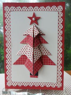 a red and white christmas card with a paper tree on the front, sitting on a table next to a window