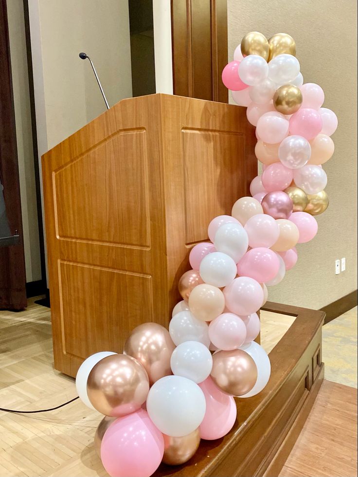 the balloon arch is decorated with pink, white and gold balloons in front of a podium