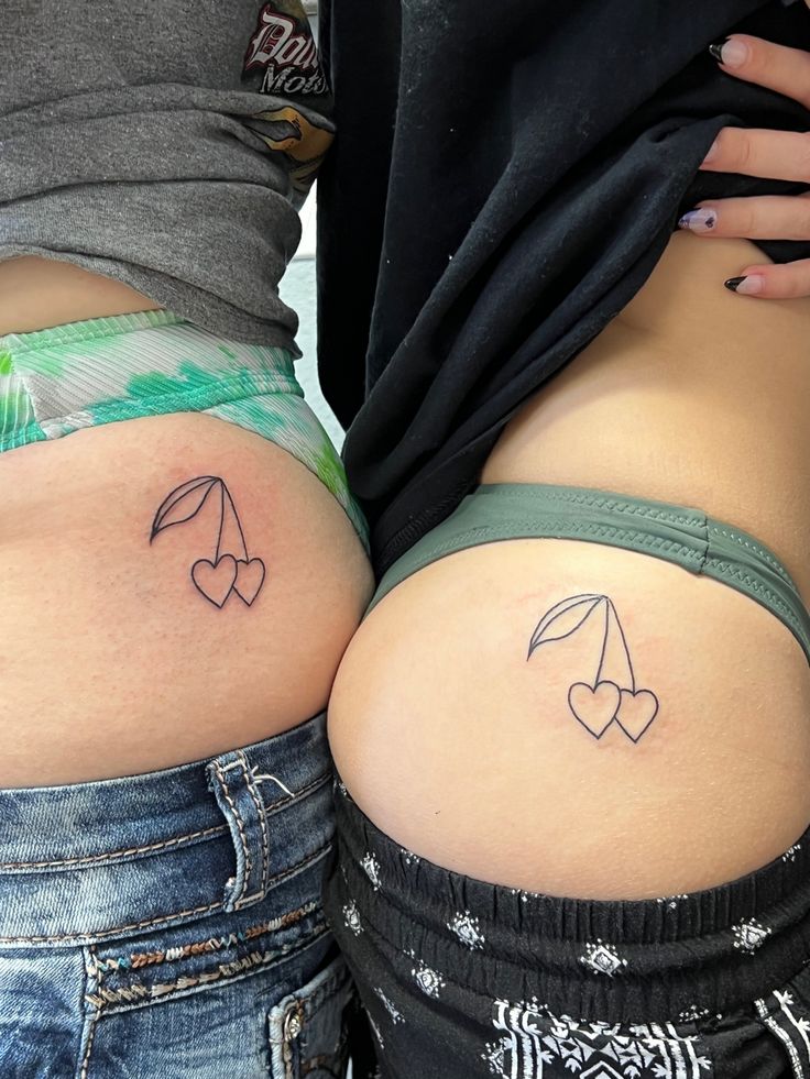 two women with small tattoos on their butts, one has an umbrella and the other has hearts