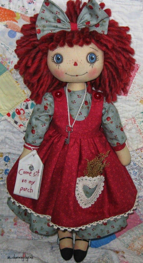 a doll with red hair and blue eyes is sitting on a quilt