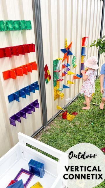 two young children playing with colorful plastic blocks in the grass next to a building made out of legos