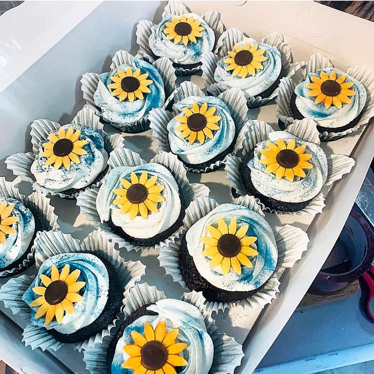 cupcakes with frosting and sunflower decorations are in a box on the table