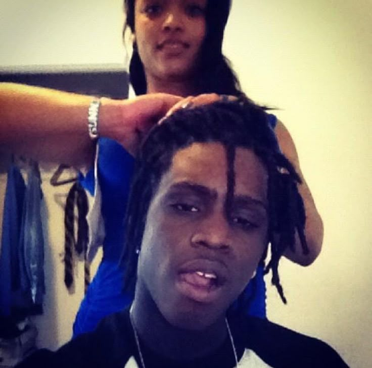 a man getting his hair cut by a woman in front of him with dreadlocks