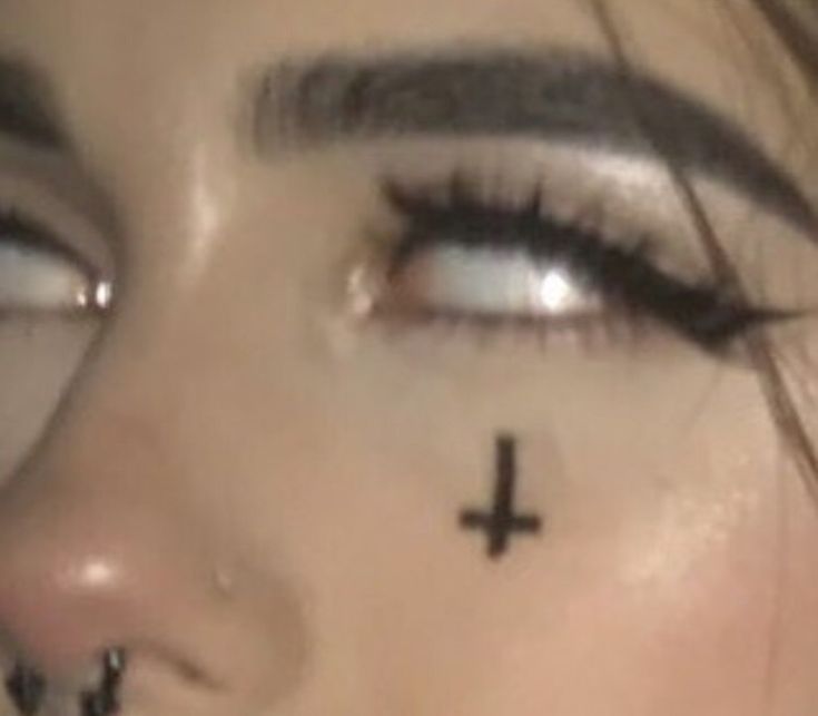 a woman with cross tattoo on her forehead and nose looking at the camera while wearing black eyeliners