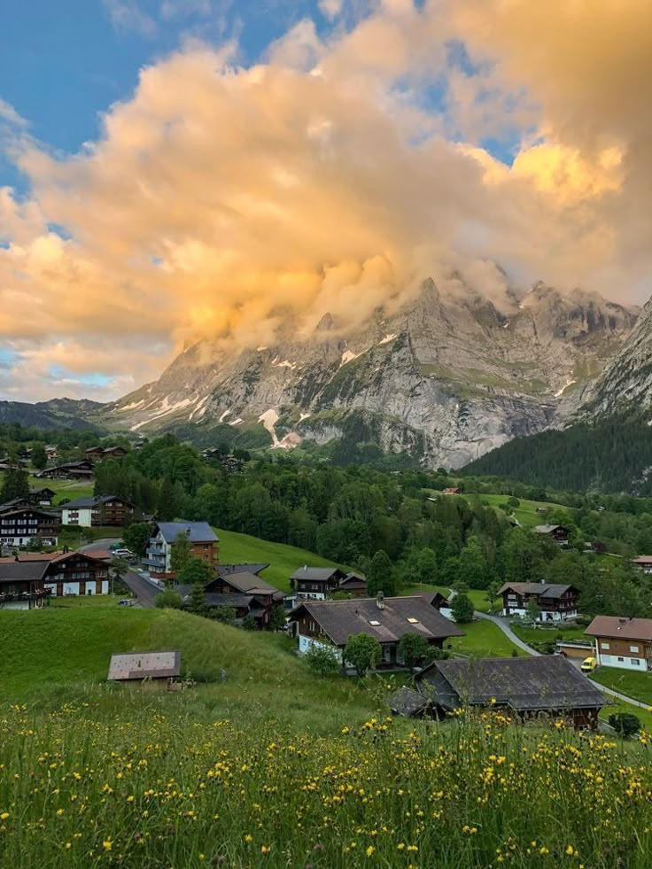 an alpine village with mountains in the background under a cloudy sky and sunbeams