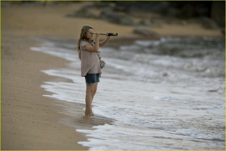 a woman standing on top of a sandy beach next to the ocean holding a camera