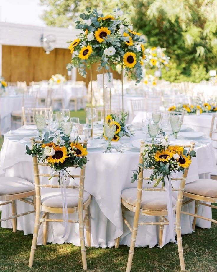 a table set up with sunflowers and greenery for an outdoor wedding reception