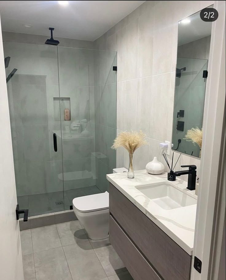 a white toilet sitting next to a bathroom sink under a mirror and a shower stall