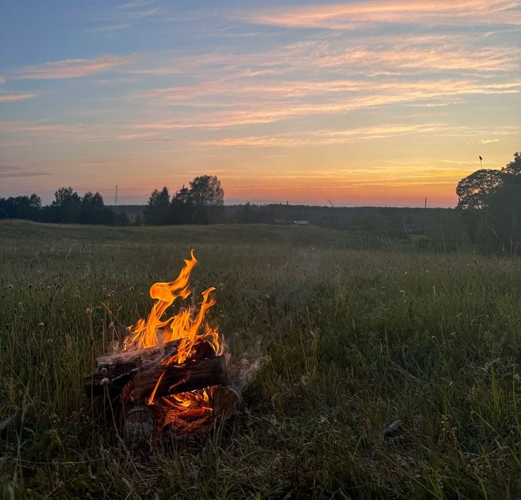 a campfire in the middle of a field at sunset