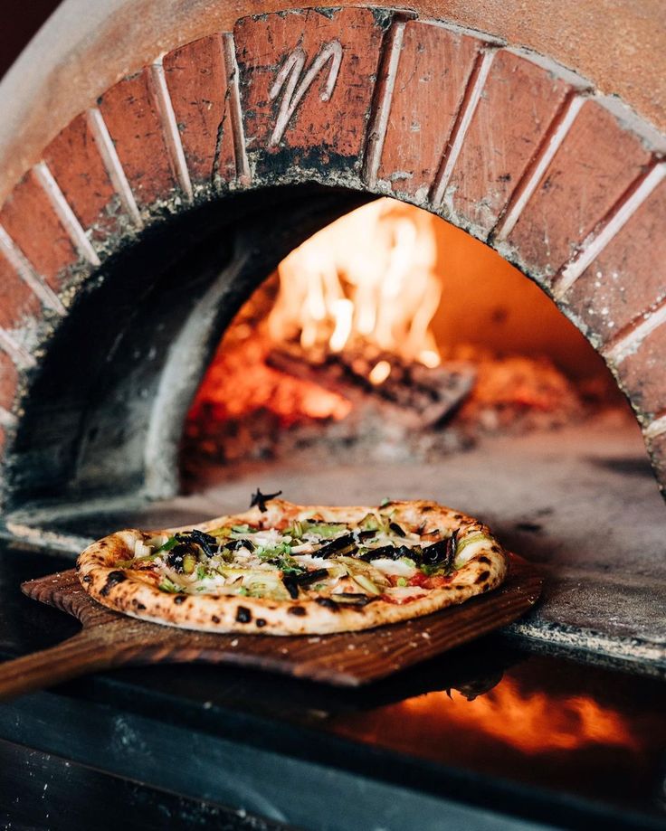 a pizza sitting in front of an oven with fire coming from it's door