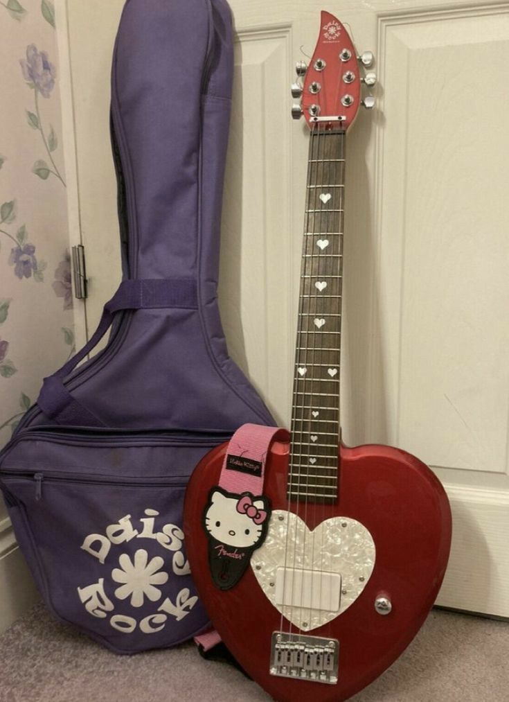 a red guitar with hello kitty on it next to a purple guitar case