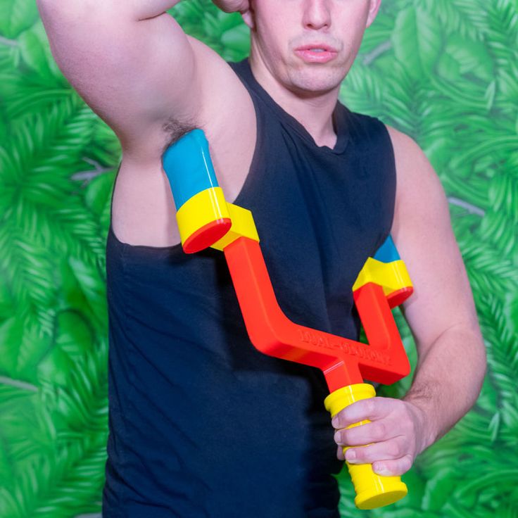 a man holding a toy in his right hand and wearing a black tank top with palm leaves behind him