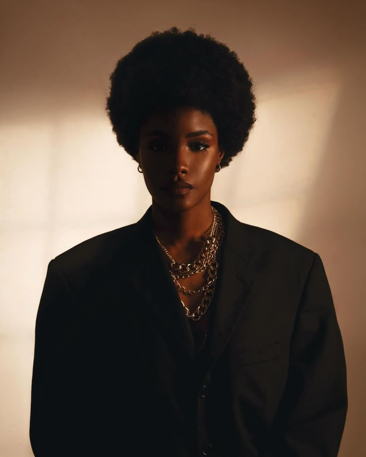 a woman with an afro standing in front of a white wall wearing a black suit