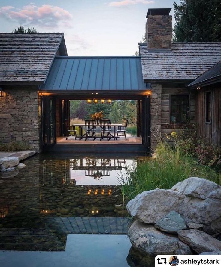 an outdoor dining area next to a pond with lights on the tables and chairs in it