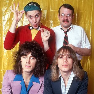 three men are posing for a photo in front of a yellow backdrop and one man is wearing a tie