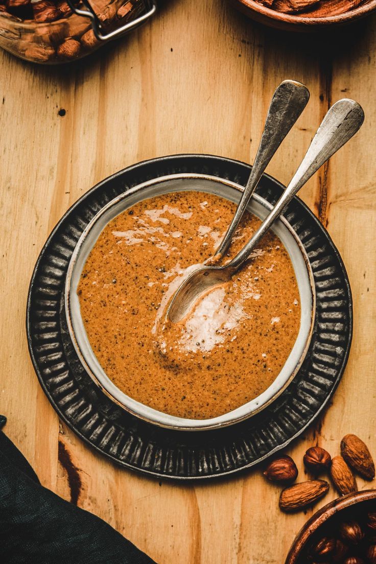 there is a bowl of soup on the table with nuts and spoons next to it