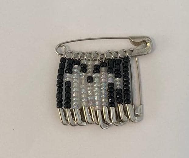 a black and white beaded brooch with silver metal clasp on a white background