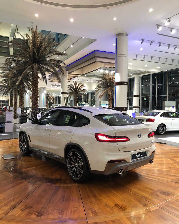 a white bmw suv is on display in a showroom with palm trees and other cars