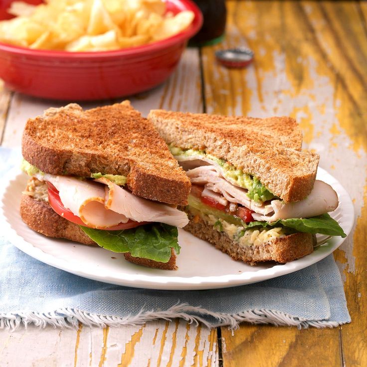 a white plate topped with a cut in half sandwich next to a bowl of chips