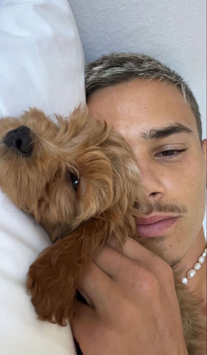 a man laying in bed with a dog on his lap and holding it up to his face