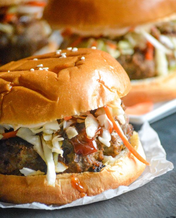 two hamburgers with meat and slaw on them are sitting on paper wrappers