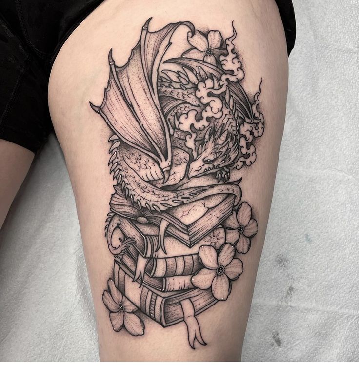 a woman's thigh with a dragon sitting on top of a pile of books