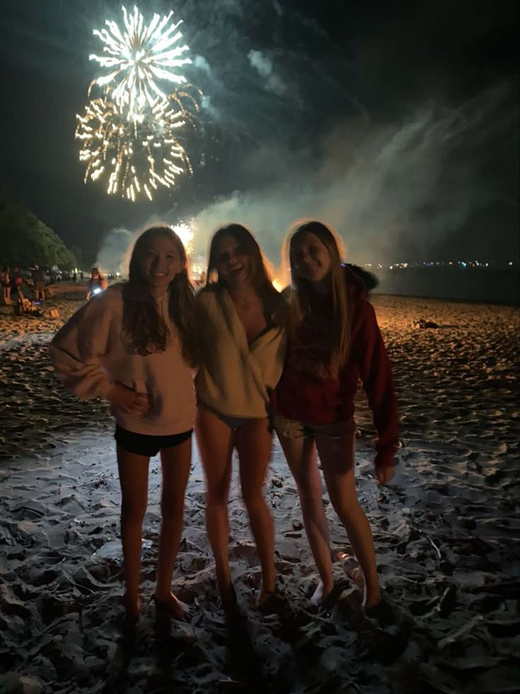 three girls standing on the beach with fireworks in the background