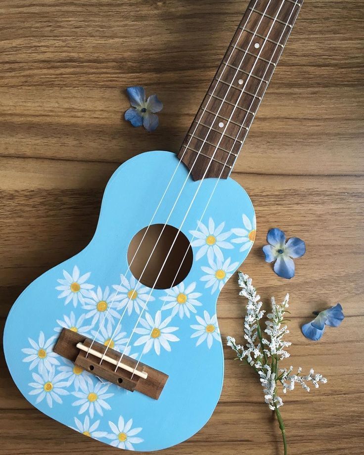 a blue ukulele with white daisies on it next to some small flowers