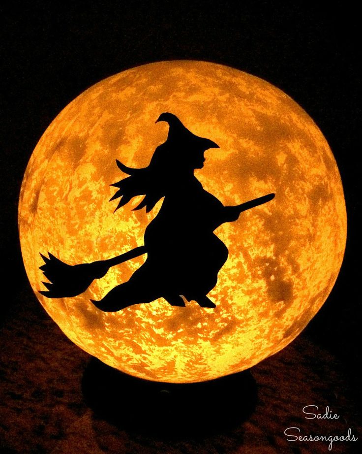 a lit up pumpkin sitting on top of a table next to a full moon with a silhouette of a witch flying over it