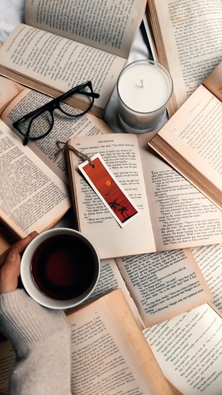 an open book and cup of coffee on top of a bed with books scattered around it