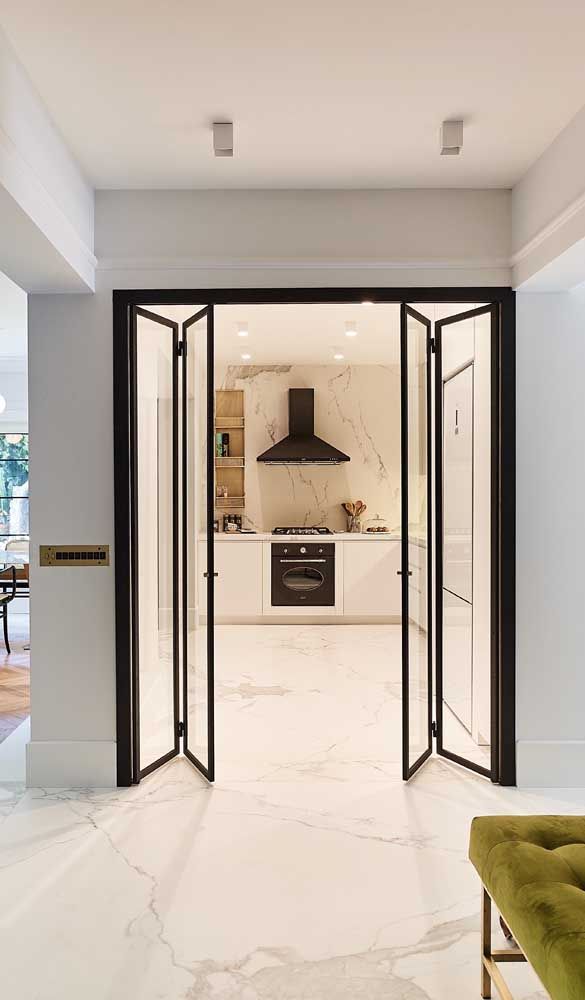 an open door leading to a kitchen and living room with white marble flooring on the walls