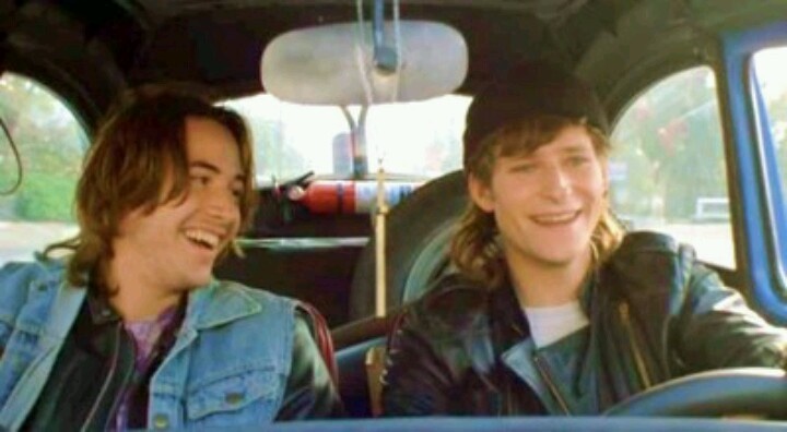 two young men sitting in the back of a car, one smiling at the camera