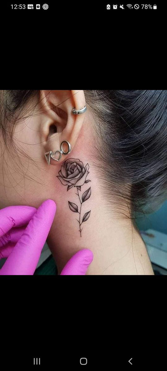 a woman's neck with a rose tattoo on her left side behind the ear