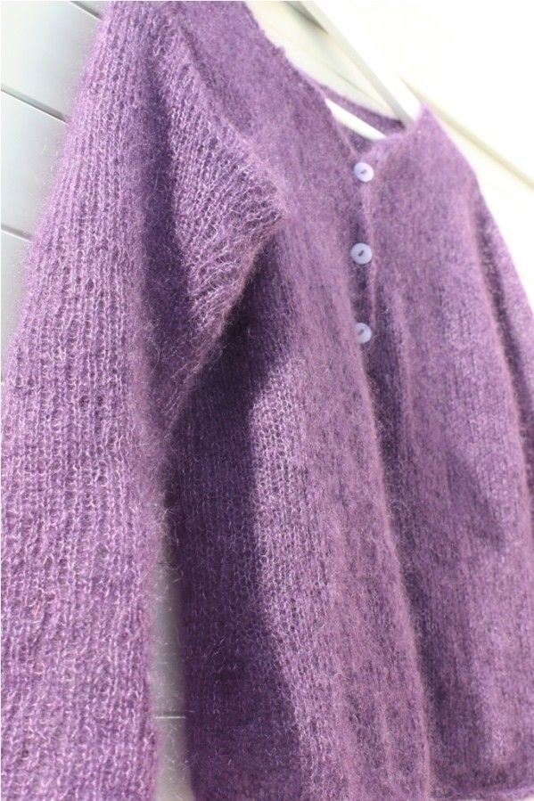 a purple sweater hanging up against a white wall next to a wooden hanger with buttons on it