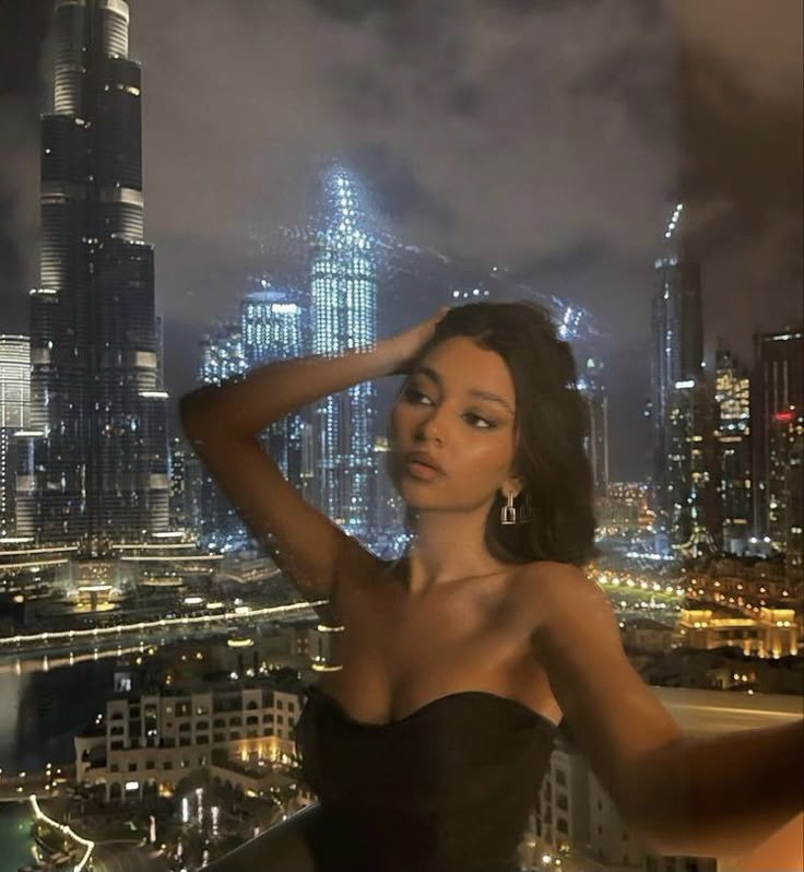 a woman standing in front of a city at night with her hand on her head