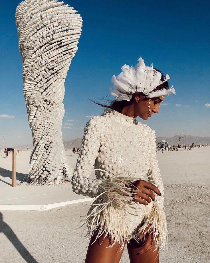 a woman standing in the desert wearing a white dress and feathered headdress