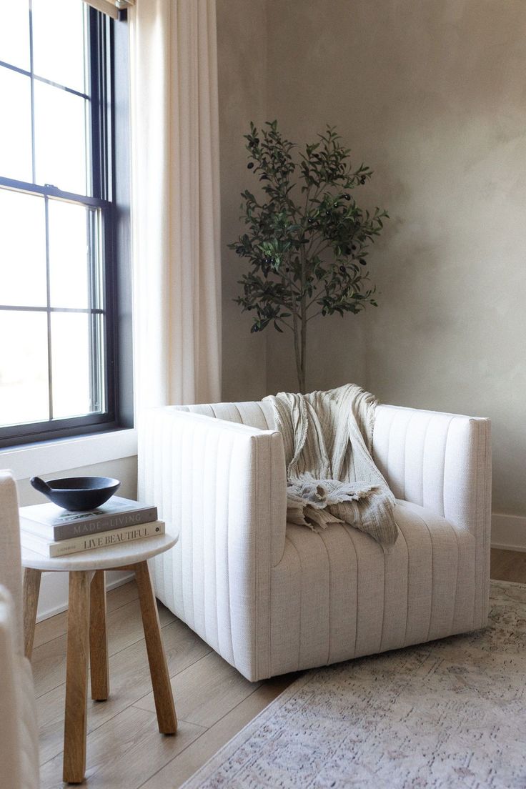 a living room with a white chair and a potted tree in the corner on top of it