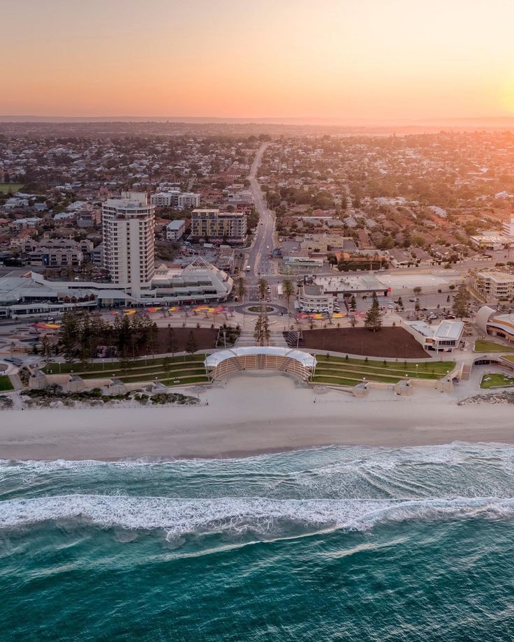 an aerial view of the beach and ocean at sunset, with buildings in the background