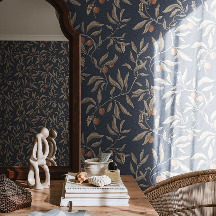 a wooden table topped with books next to a wallpaper covered in leaves and berries