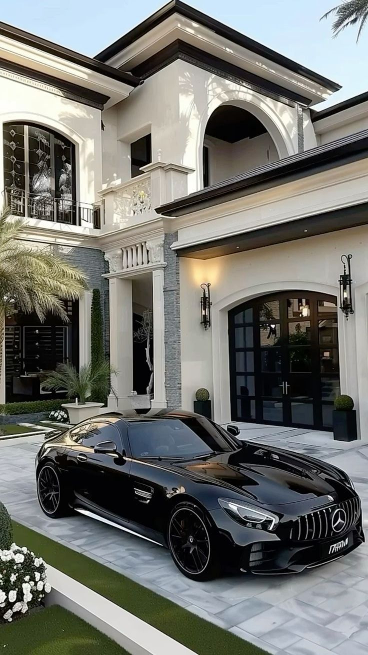 a black sports car is parked in front of a large white house with palm trees