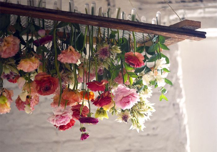 an arrangement of flowers hanging from a wooden beam in a room with white brick walls