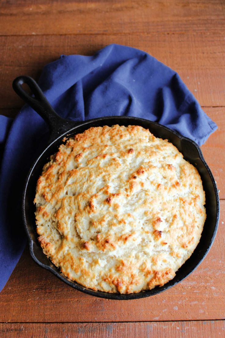 a cast iron skillet filled with food on top of a wooden table next to a blue napkin