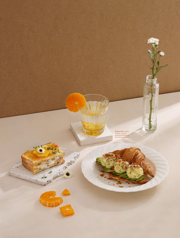 there is a white plate with food on it next to a glass and flower vase