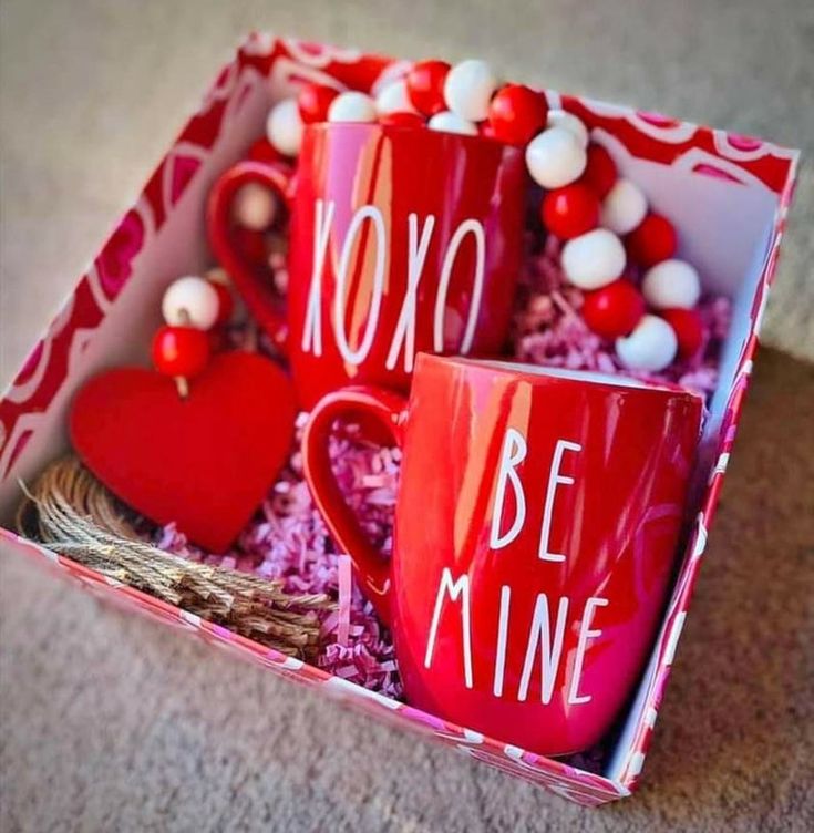 two red coffee mugs sitting in a box with candy balls on the floor next to it