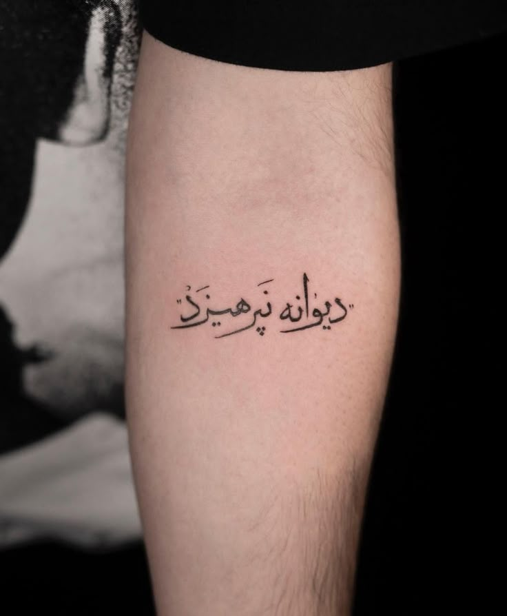 a tattoo with arabic writing on the left arm and lower leg, in black ink